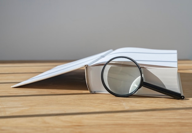 Vergrootglas met open dik boek op houten bureau met daglicht