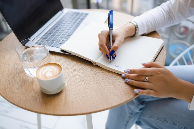 Vergrote weergave van de handen van een vrouw die notities schrijft in een notitieblok. meisje werkt in een café