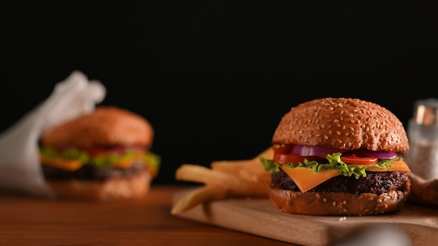 Vergrote weergave van heerlijke gegrilde rundvleesburgers geserveerd op houten dienblad op de tafel met zwarte muur