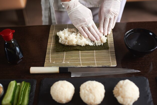 Vergrote weergave van proces ter voorbereiding van rollende sushi. Nori en witte rijst. De vrouwelijke handen van de chef raken rijst aan. Chef begint sushi te koken