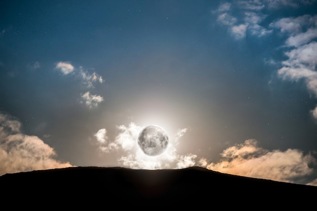 Verhoging van de volle maan boven de berg bij donkerblauwe nachtelijke hemel met sterren