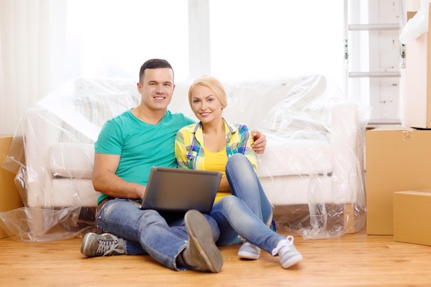 verhuizen, huis, technologie en koppel concept - lachend paar met laptop zittend op de vloer in nieuw huis