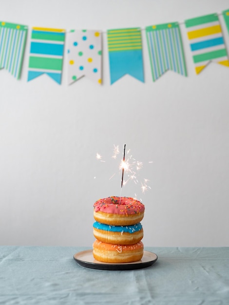 verjaardag donuts taart met bengal licht of sparkler Stapel heerlijke donuts over tafel met partij vlag krans op de achtergrond Verticale kopie ruimte