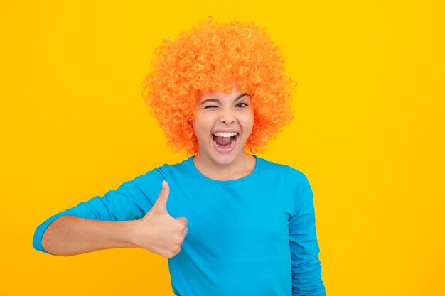 Verjaardag kinderfeestje Grappige jongen in krullende clown pruik geïsoleerd op gele achtergrond Opgewonden tiener blij verbaasd en dolblij emoties