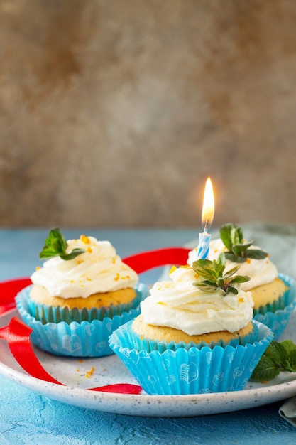 Verjaardagscupcake met slagroompapaver en sinaasappelschil op een blauwe achtergrond