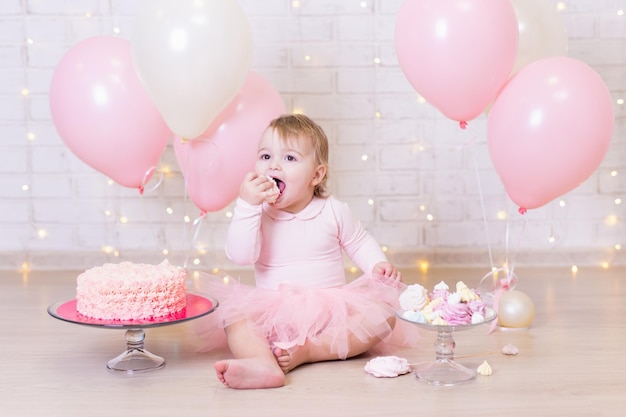 Verjaardagsfeestje concept - grappig meisje taart eten over bakstenen muur achtergrond met lichten en kleurrijke ballonnen