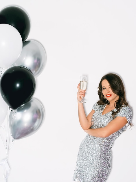 Verjaardagsfeestje Stijlvolle vrouw Feestelijke foto Vakantiefeest Mooie gelukkige dame in lovertje zilveren jurk poseren met glas champagne geïsoleerde witte kleurrijke ballonnen