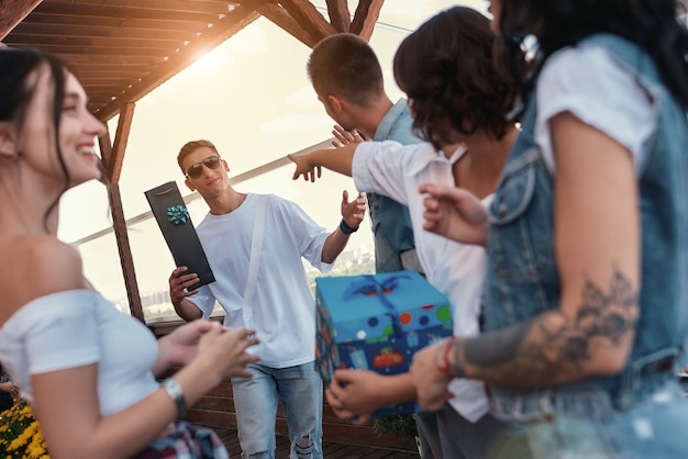 Verjaardagsfeestje vrolijke jonge mensen die geschenken vasthouden en genieten van een feestje op het dak terwijl