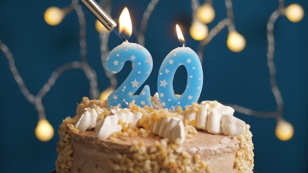 Verjaardagstaart met 20 nummerkaars op blauwe achtergrond in brand gestoken door aansteker. Detailopname