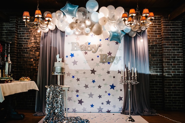 Verjaardagstaart op een achtergrond blauwe, witte en zilveren ballonnen, bakstenen muur. Baby shower partij, decor. Taart met figuurkoets voor een jongen. Ruimte kopiëren. Viering doopconcept.