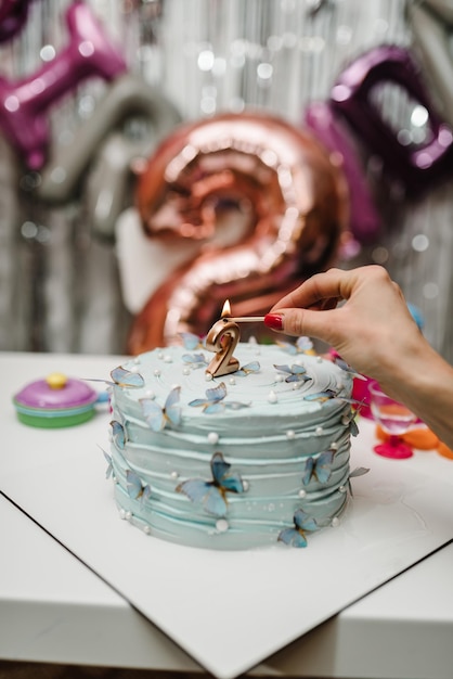 Verjaardagstaart voor 2 jaar op een achtergrond van ballonnen De taart is versierd met vlindersfiguren en kaarsdecor Het concept van feestelijke desserts