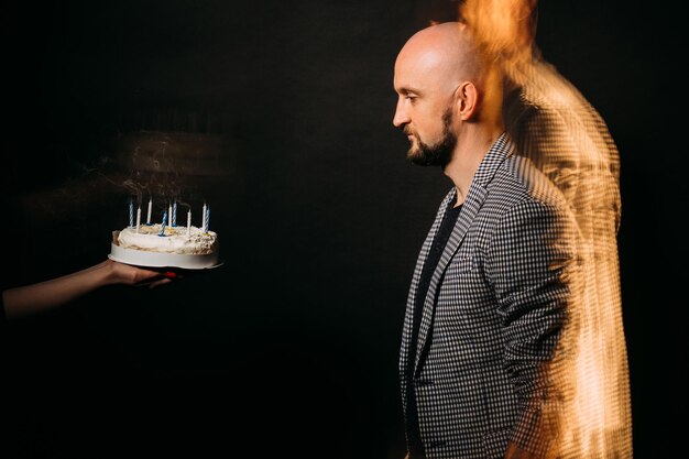 Verjaardagswens Ernstige man Feestelijke bakkerij Feestviering Geconcentreerde hipster kerel op zoek naar vakantie cake met kaarsen rook geïsoleerde zwarte lange blootstelling intreepupil vorm kopie ruimte