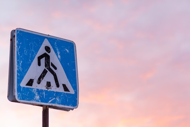 Verkeersbord voetgangersoversteekplaats op de achtergrond van de hemel. Een versleten bord op de achtergrond van zonsondergang waarschuwt automobilisten voor een zebrapad. Voorzichtigheid op de weg.