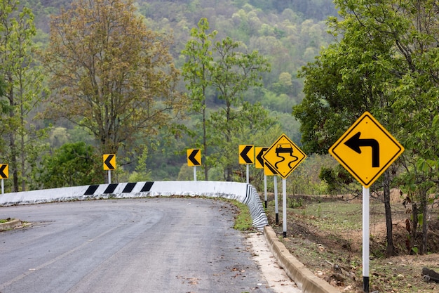 Verkeersbord voorzichtigheid die aangeeft dat de bocht naar links en het gevaar van een gladde weg op de berg