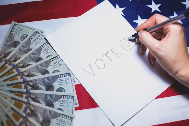 Foto verkiezingen in de vs. vrouw zet een vinkje op het papier om te stemmen. politieke veranderingen in het land. corruptie systeem. amerikaanse vlag en dollarsgeld. mensen stemmen op de stemming.