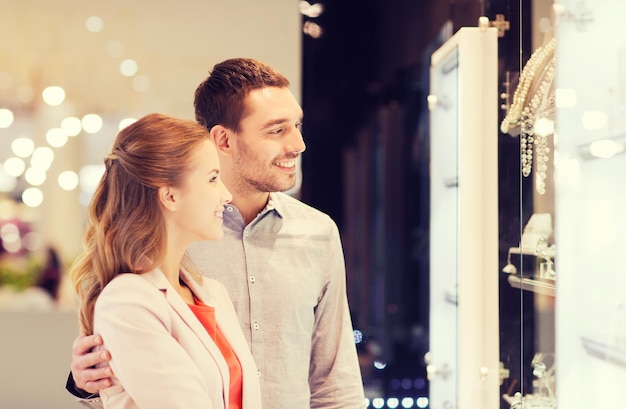 verkoop, consumentisme en mensenconcept - gelukkig paar wijzende vinger naar etalage bij juwelier in winkelcentrum