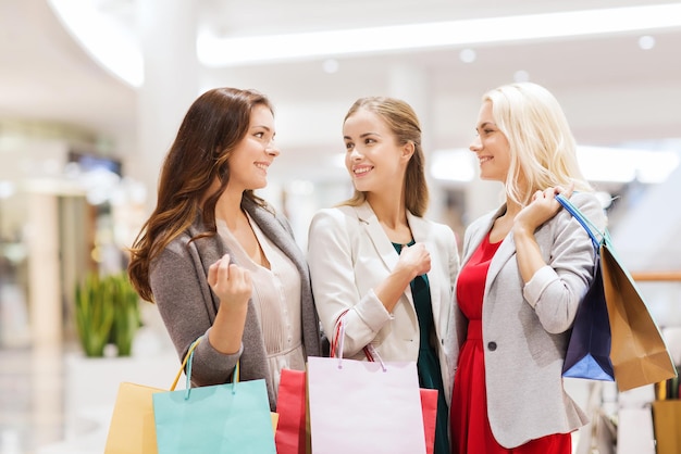 verkoop, consumentisme en mensenconcept - gelukkige jonge vrouwen met boodschappentassen die in winkelcentrum praten