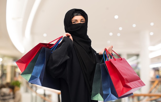 verkoop, consumentisme en mensenconcept - moslimvrouw in hijab met boodschappentassen over winkelcentrumachtergrond