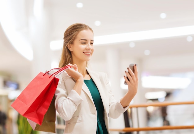 verkoop, consumentisme, technologie en mensenconcept - gelukkige jonge vrouw met smartphone en boodschappentassen die selfie in winkelcentrum nemen