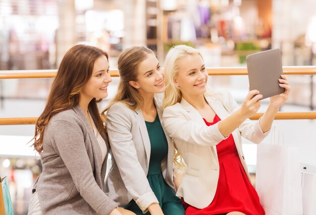 verkoop, consumentisme, technologie en mensenconcept - gelukkige jonge vrouwen met tablet-pc en boodschappentassen in winkelcentrum