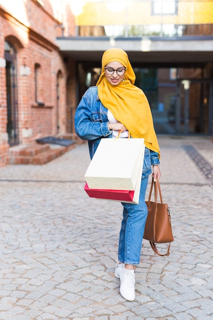 Verkoop en kopen concept - gelukkig arabisch moslimmeisje met boodschappentassen na winkelcentrum