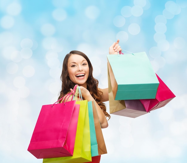 verkoop, geschenken, vakanties en mensen concept - lachende vrouw met kleurrijke boodschappentassen over blauwe lichten achtergrond