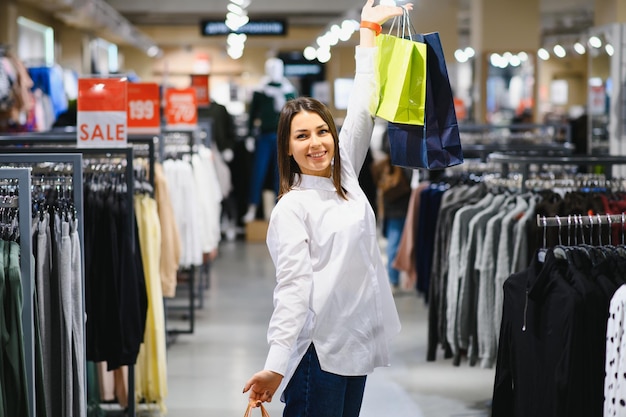Verkoop, kleding, winkelen, mode en mensen concept - gelukkige jonge vrouw kiezen tussen twee shirts in winkelcentrum of kledingwinkel