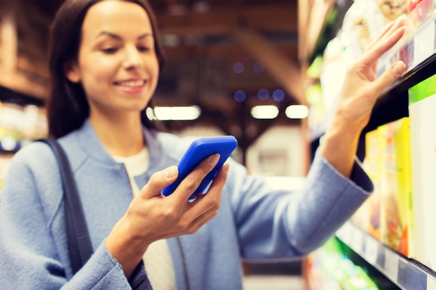 verkoop, winkelen, consumentisme en mensenconcept - gelukkige jonge vrouw met smartphone die voedsel op de markt kiest en koopt