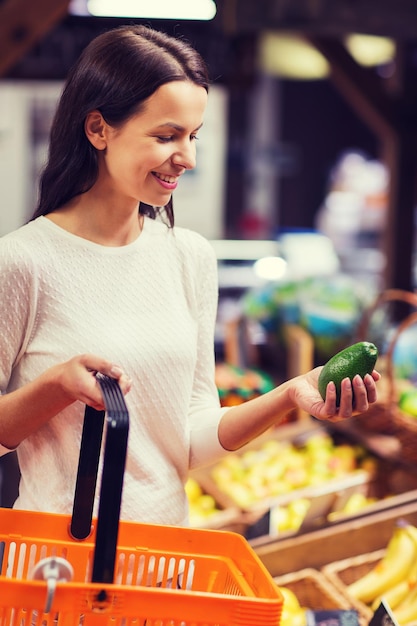 verkoop, winkelen, consumentisme en mensenconcept - gelukkige jonge vrouw met voedselmand die komkommer in markt houdt