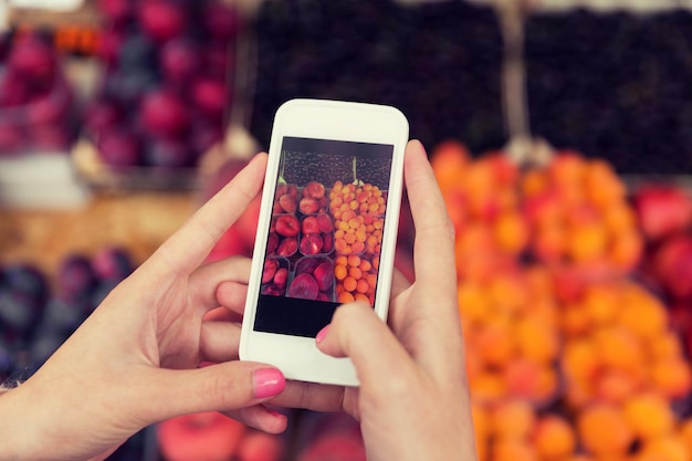 verkoop, winkelen, eten, technologie en mensenconcept - close-up van handen met smartphone die foto's maakt van fruit op straatmarkt