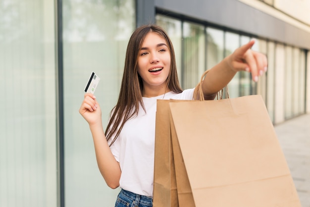 Verkoop, winkelen, toerisme en gelukkige mensen concept - mooie vrouw met boodschappentassen en creditcard in de handen op een straat