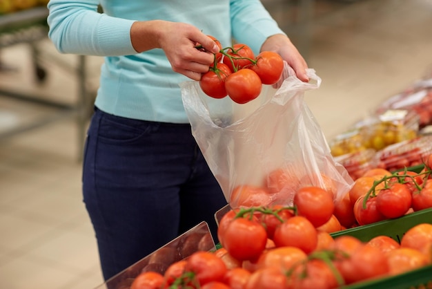 verkoop, winkelen, voedsel, consumentisme en mensenconcept - vrouw met tas die tomaten koopt in de supermarkt