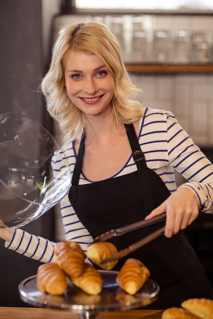 Verkoper die een croissant met tang plukt