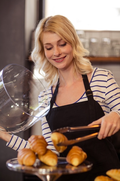 Foto verkoper die een croissant met tang plukt