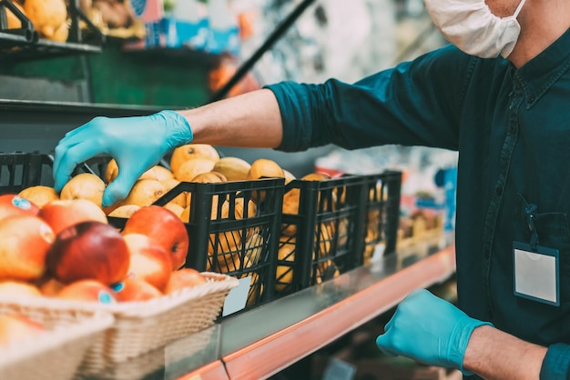 Verkoper met een beschermend masker staat voor de toonbank met fruit. coronavirus in de stad