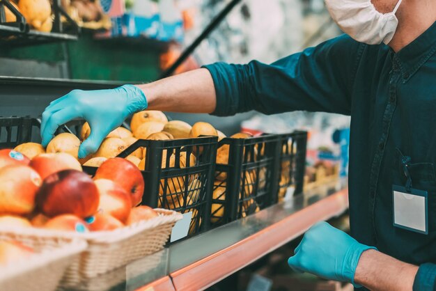 Verkoper met een beschermend masker staat voor de toonbank met fruit