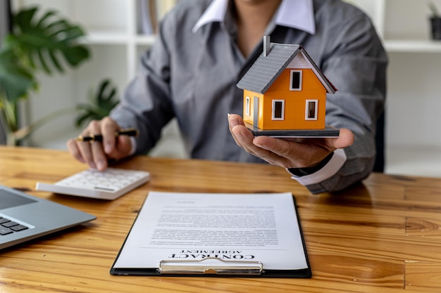 Verkoper met een oranje model van een klein huis, een verkoper van een woningbouwproject stelt een verkoopcontract op voor een klant die een huis reserveert in een project dat hij onderhoudt. Vastgoed handelsconcept.