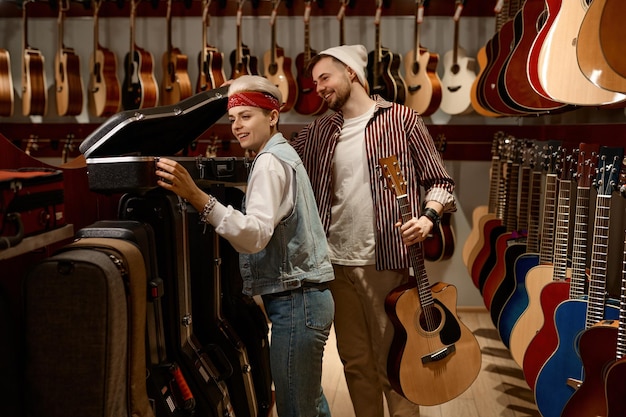 Verkopersvrouw die mankoper helpt bij het kiezen van een gitaarkoffer in de muziekwinkel