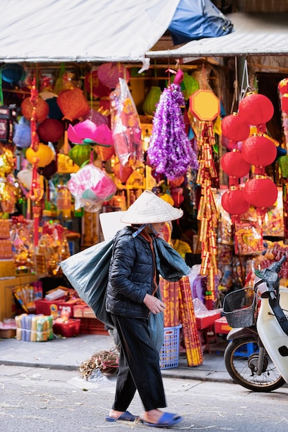 Verkopersvrouw draagt traditionele Vietnamese hoed op straatmarkt in de oude stad Hanoi in Azië in Vietnam. Winkel met lantaarns. Lokale zakelijke handel met koopwaar tentoongesteld in de winkel.