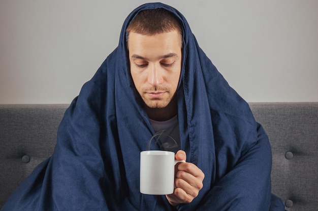 Verkoudheid en griep Portret van een zieke jonge kerel die thee drinkt in bed zieke blanke zittend met een kop warme drank in zijn handen met koorts die zich niet goed voelt thuis close-up