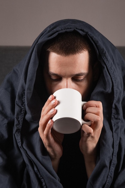 Verkoudheid en griep Portret van een zieke jonge kerel die thee drinkt in bed zieke blanke zittend met een kop warme drank in zijn handen met koorts die zich niet goed voelt thuis close-up