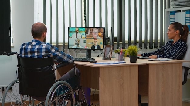 Verlamde, geïmmobiliseerde freelancer in rolstoel met videovergadering die online bespreekt met collega's in het kantoor. Gehandicapte zakenman die werkt in een financieel bedrijf met behulp van moderne technologie.