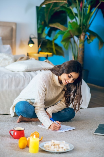 Verlanglijst. Vrouw zittend op de vloer en haar verlanglijst schrijven