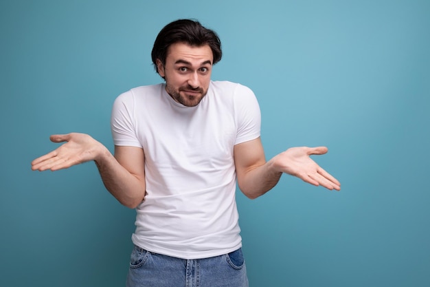 Verlegen jonge brunette man in witte t-shirt op studio achtergrond