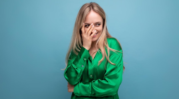 Verlegen vrouw in groen shirt poseren op blauwe studio achtergrond