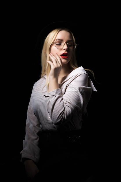 Verleidelijke jonge blonde vrouw in glazen poseren met dramatische studio licht