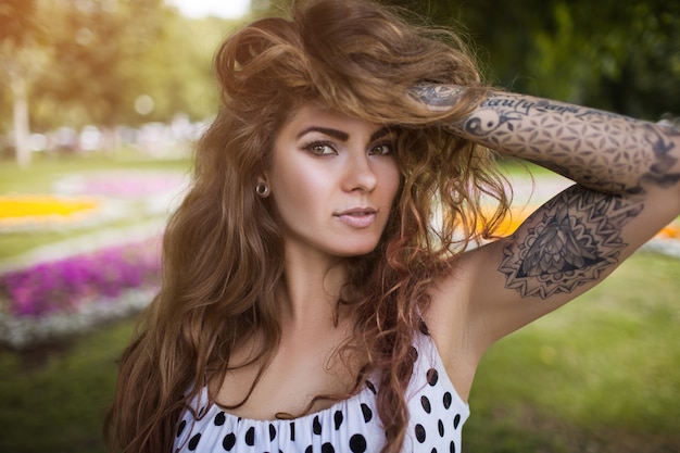 Foto verleidelijke jonge vrouw met krullend wild haar en tatoeages.