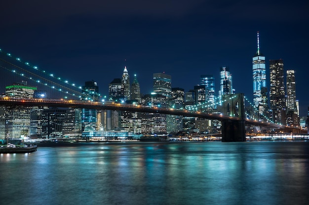 Verlichte brooklyn brug over de rivier tegen gebouwen's nachts