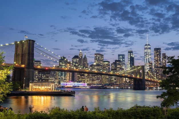 Verlichte brooklyn brug over de rivier tegen gebouwen's nachts