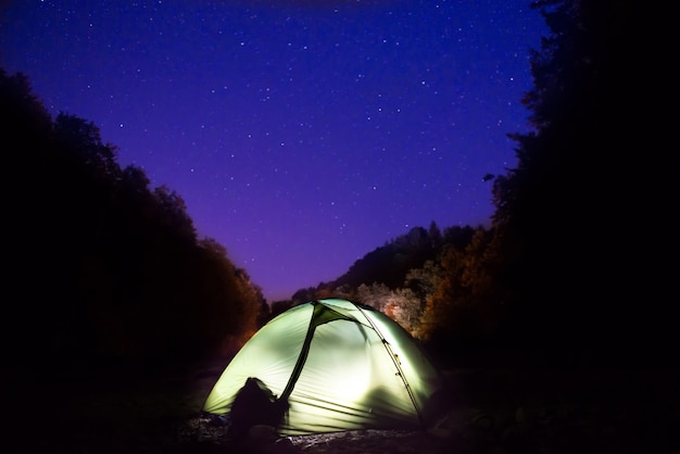 Verlichte groene tent 's nachts in het bos onder donkerblauwe lucht met veel sterren